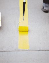 A view of a person repainting the parking lines of the asphalt of a parking lot with yellow paint